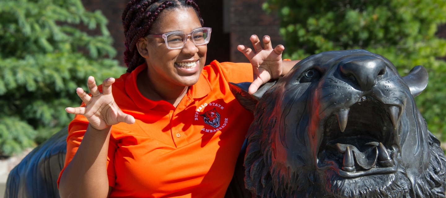 Student standing next to tiger statue holding hands like claws